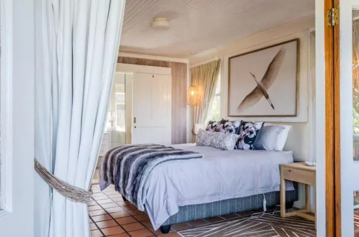 Bright bedroom with queen bed, patterned pillows, and coastal artwork above