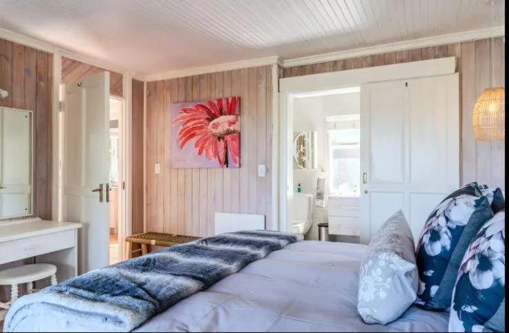 Bright bedroom with queen bed, wooden walls, pink flower artwork, ensuite access