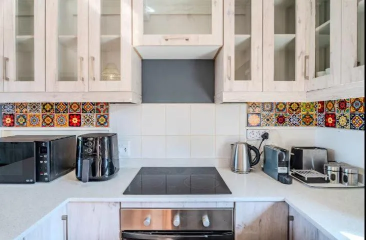 Modern kitchen with white cabinetry, colorful tile backsplash, and stainless steel appliances