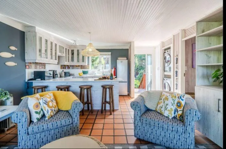 Open-plan lounge with blue armchairs facing kitchen and dining area