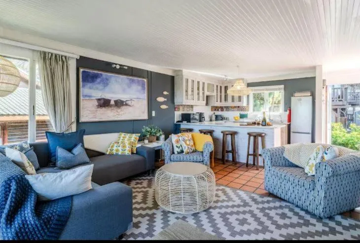 Open-plan lounge with blue sofas, beach artwork, and kitchen visible beyond