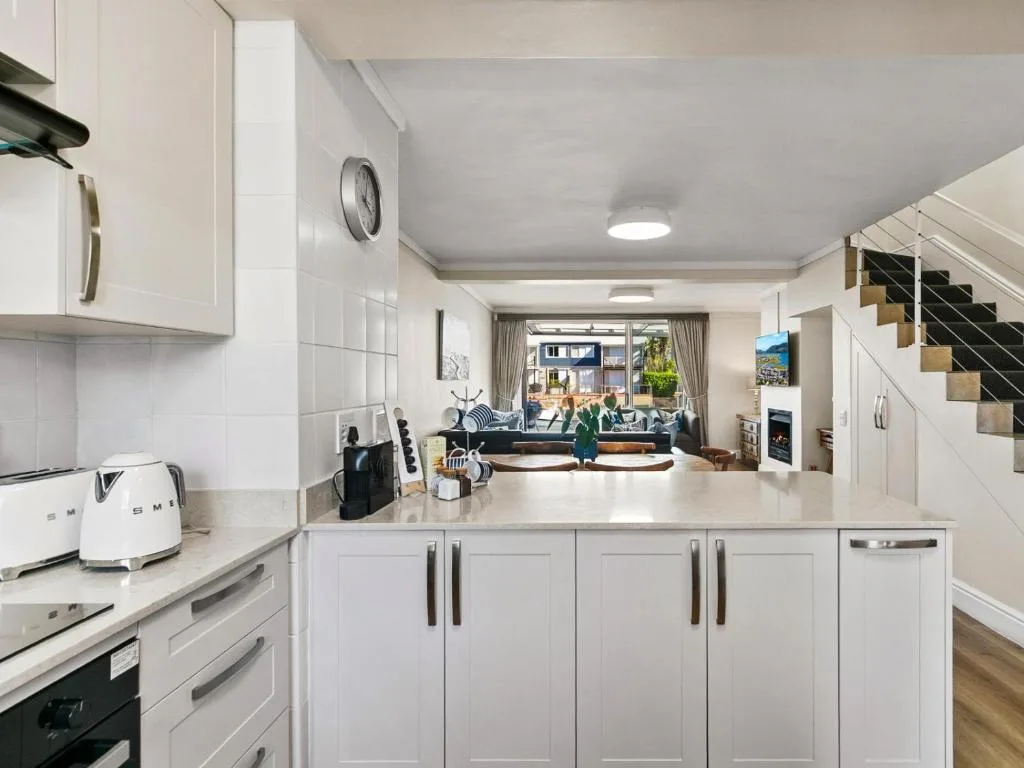 Modern white kitchen with countertop, appliances, and open-plan living area beyond