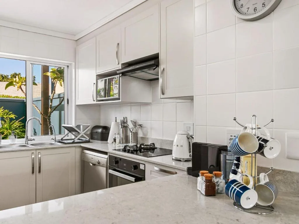 Modern white kitchen with stainless steel appliances and garden view