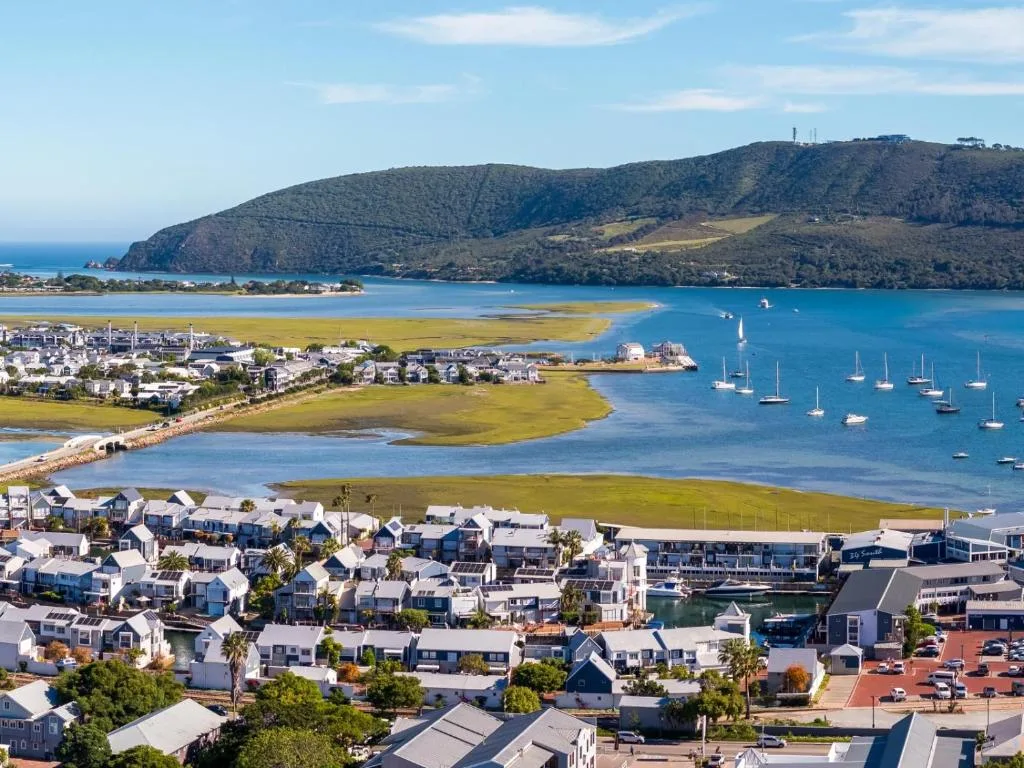 Aerial view of Knysna Lagoon with white buildings, sailboats, and forested mountains