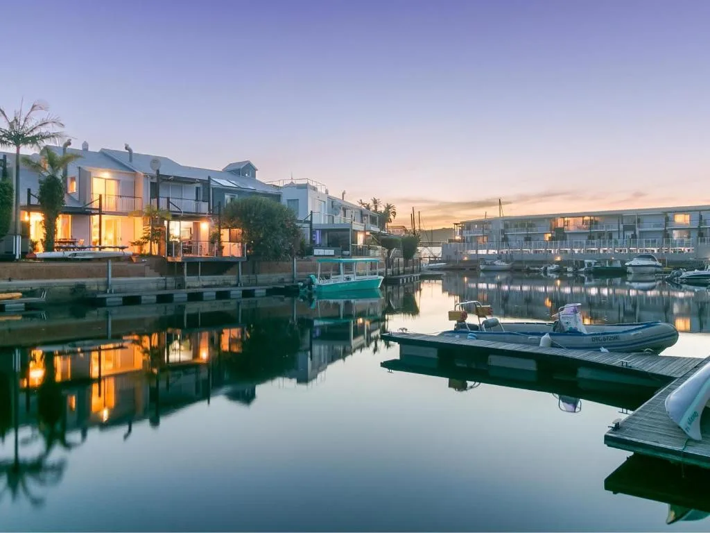 Waterfront homes and boats reflected in calm lagoon water at dusk