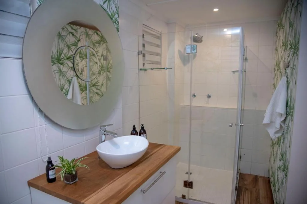 Modern bathroom with round mirror, white vessel sink, wooden vanity, and walk-in shower