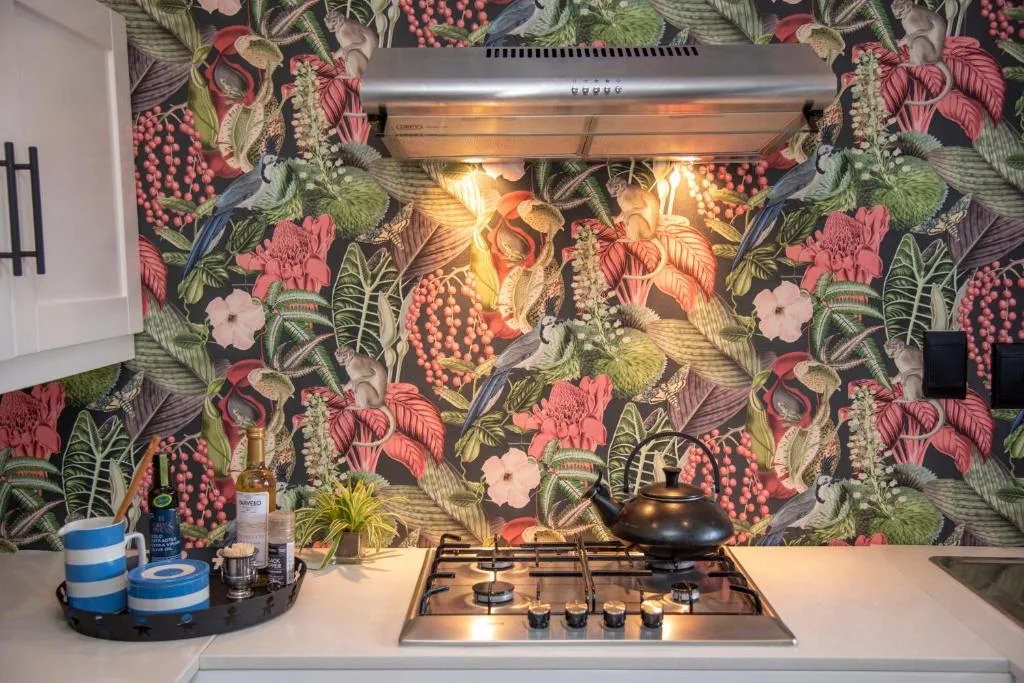 Modern kitchen with gas stovetop, vibrant botanical wallpaper, and stainless steel rangehood