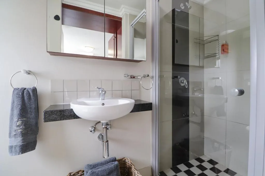 Modern bathroom with curved white sink, mirrored cabinet, and glass shower enclosure