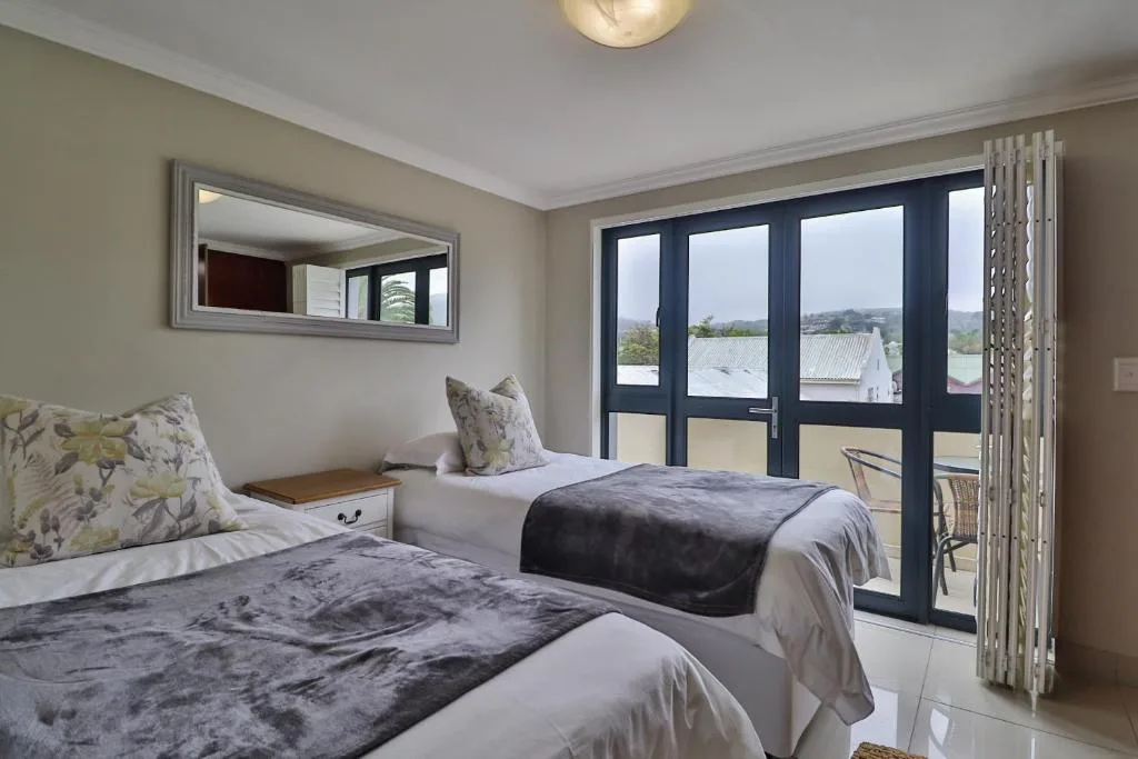 Twin bedroom with beds, mirror, and lagoon views through glass doors