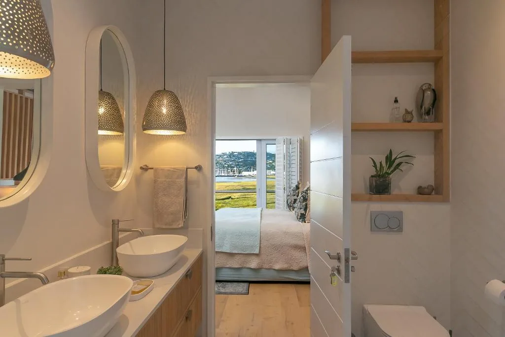 Modern bathroom with dual vanities, pendant lights, and lagoon views through open doors