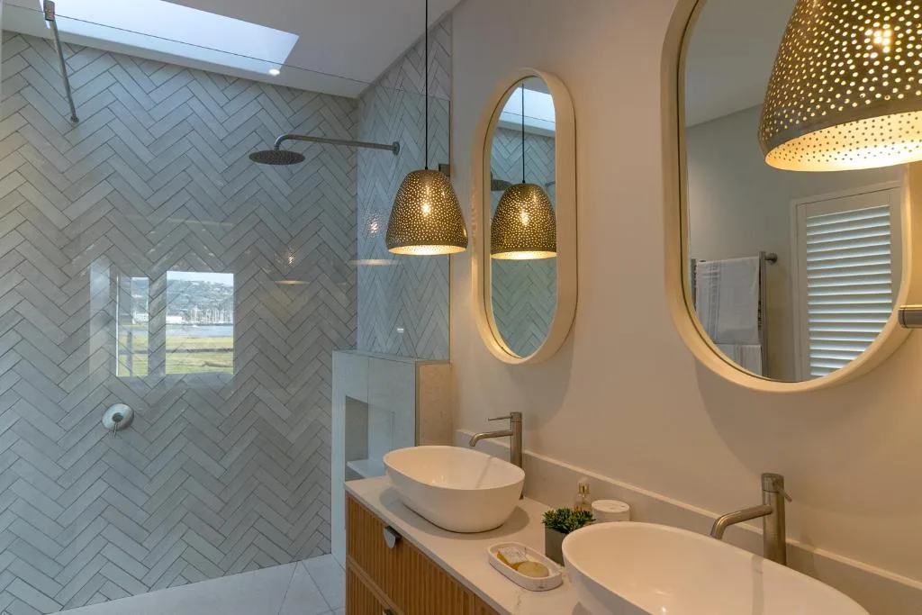 Modern bathroom with dual vessel sinks, brass pendant lights, and herringbone tile shower