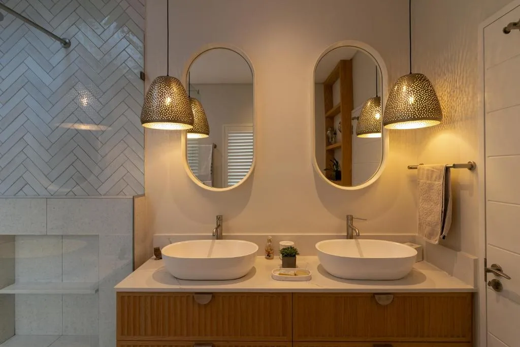 Modern double vanity bathroom with vessel sinks, arched mirrors, and brass pendant lights