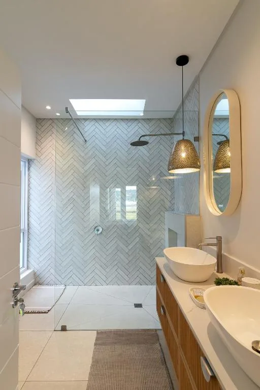 Modern bathroom with herringbone tile shower, dual vanity sinks, and pendant lights