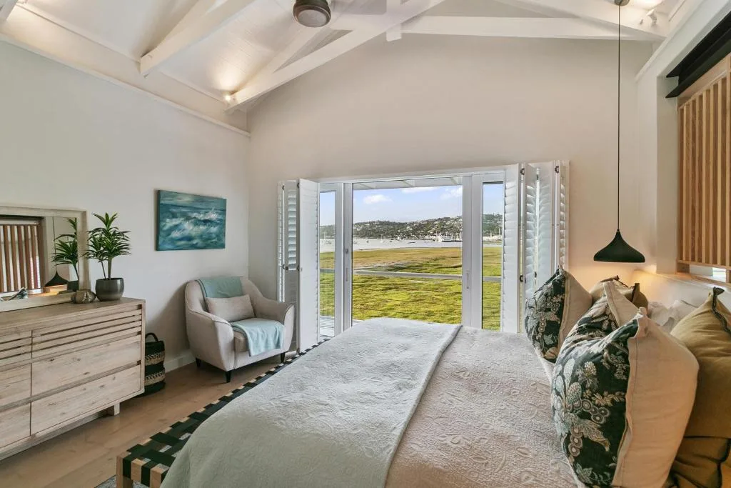 Bright bedroom with lagoon views through large glass doors and coastal landscape