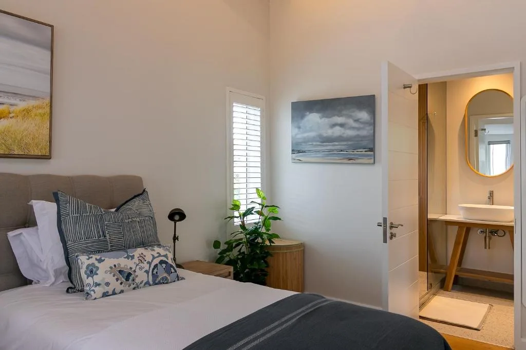 Bright bedroom with bed, pillows, ensuite bathroom visible through open door