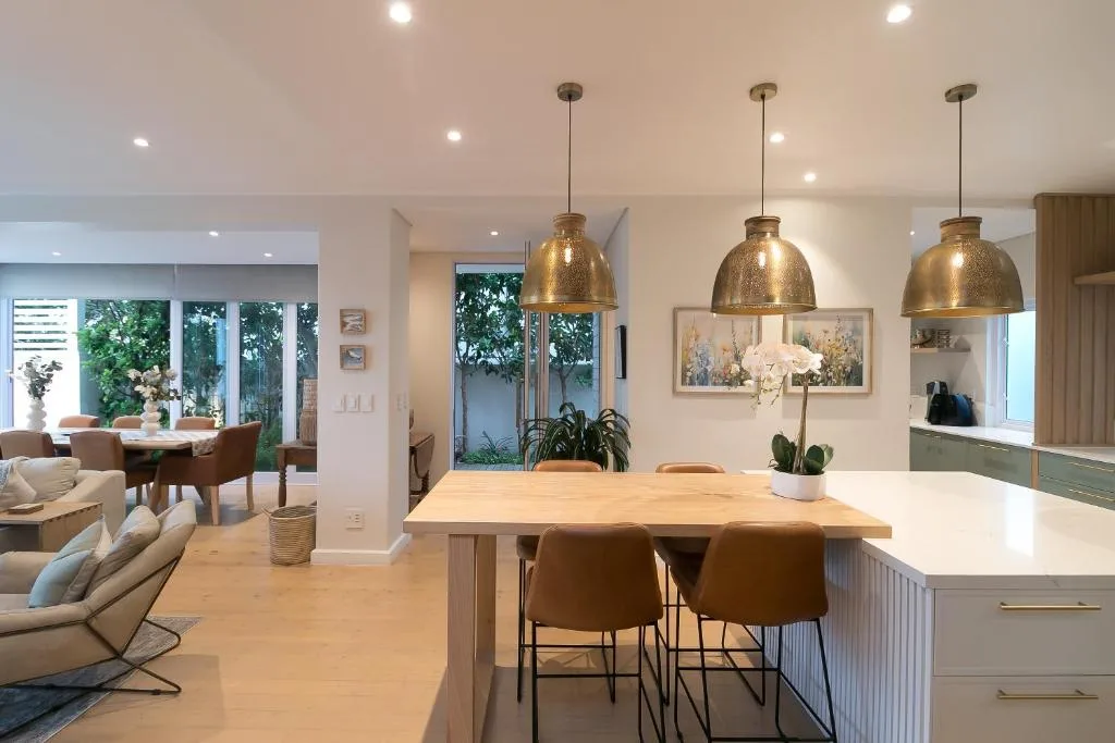 Modern dining area with wooden table, brass pendant lights, and kitchen island