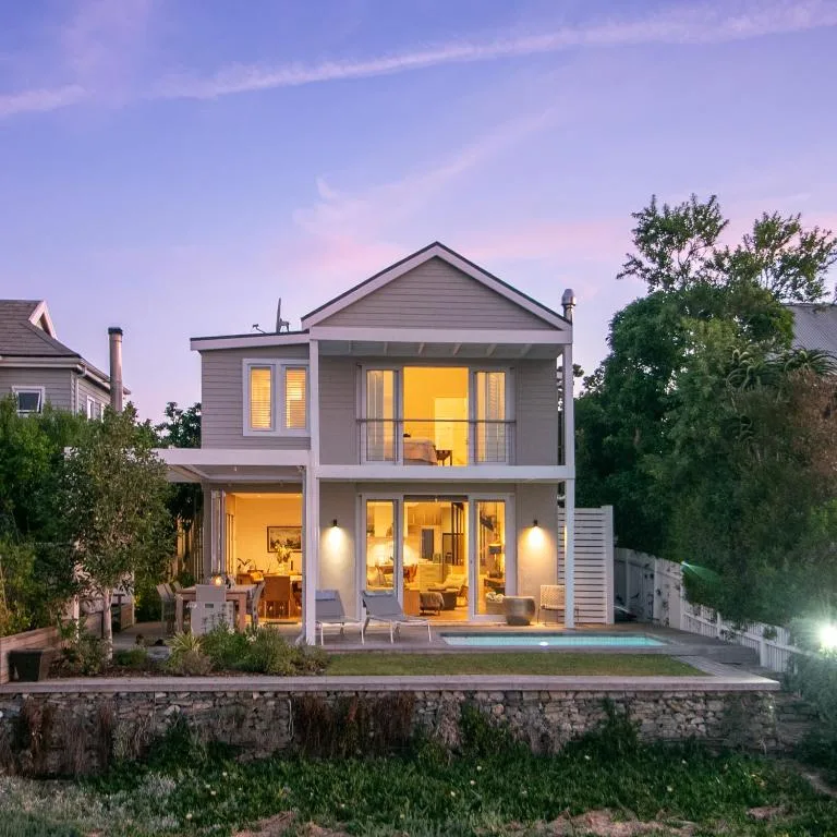 Modern two-story villa with illuminated windows at twilight, stone foundation visible