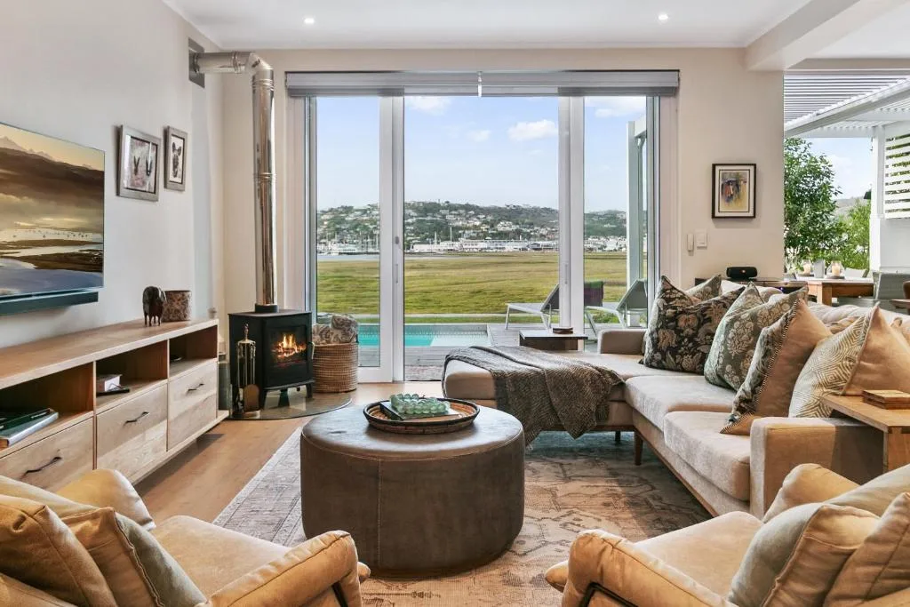 Spacious lounge with sofas, fireplace, and expansive lagoon views through glass doors