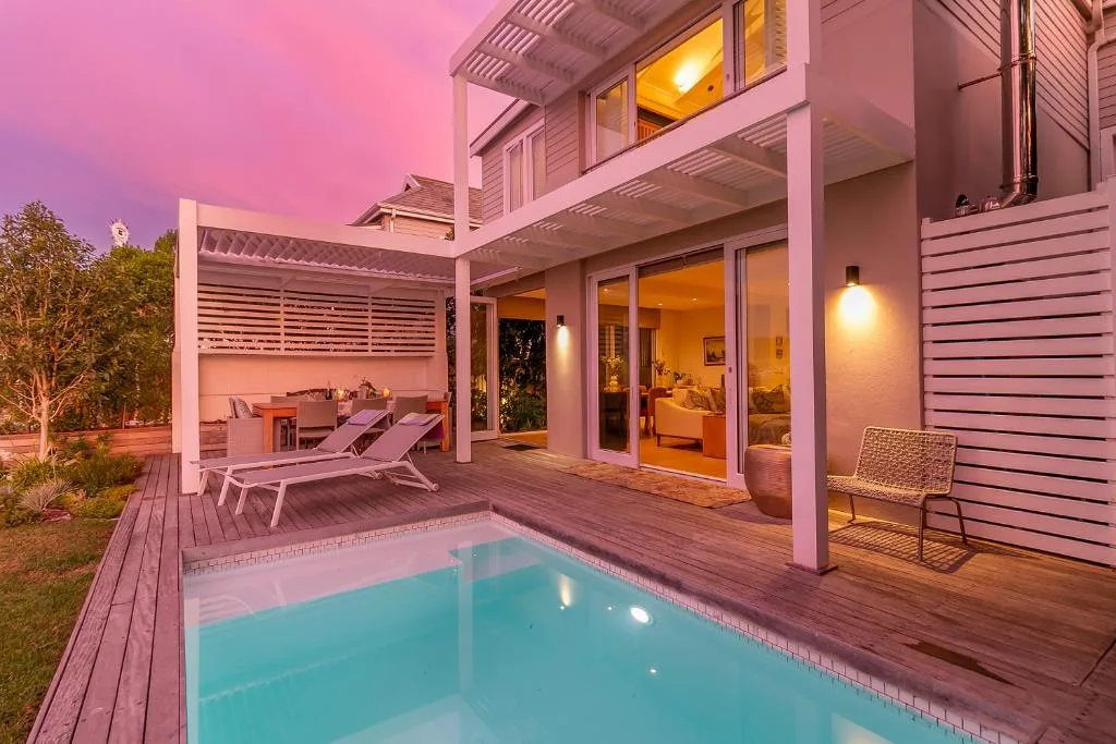 Illuminated swimming pool with wooden deck and modern villa at dusk