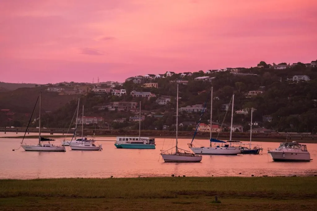 Sailboats anchored in Knysna lagoon at sunset, hillside homes visible
