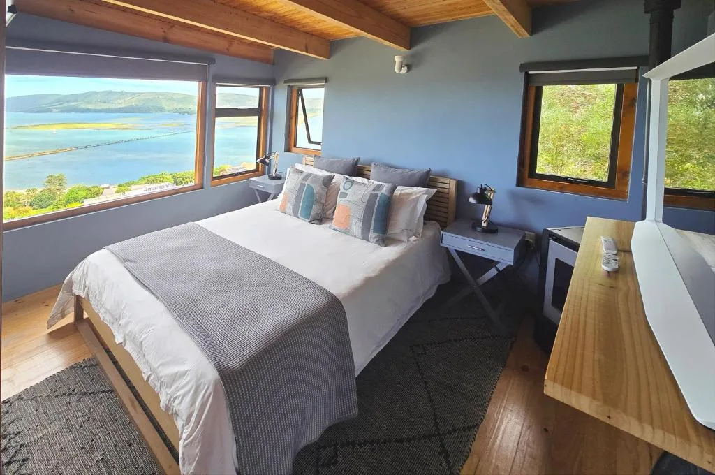 Bedroom with queen bed, wooden beams, and panoramic lagoon views through large windows
