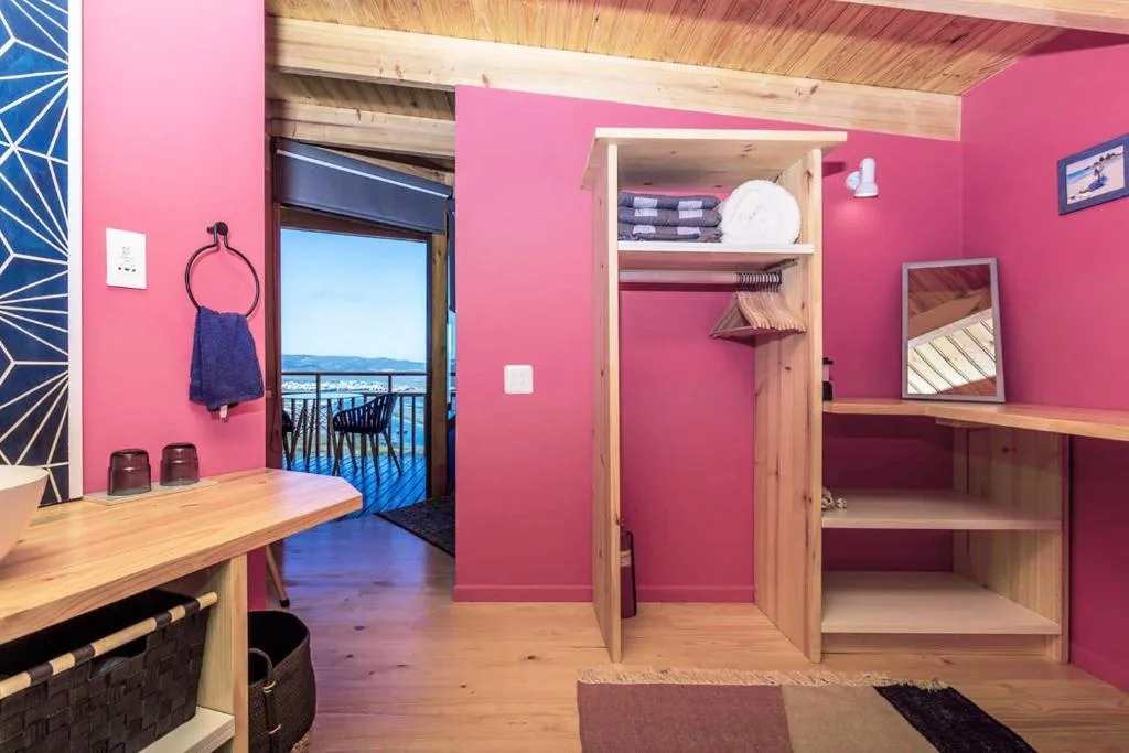 Bright pink bedroom with wooden wardrobe and ocean view through glass door