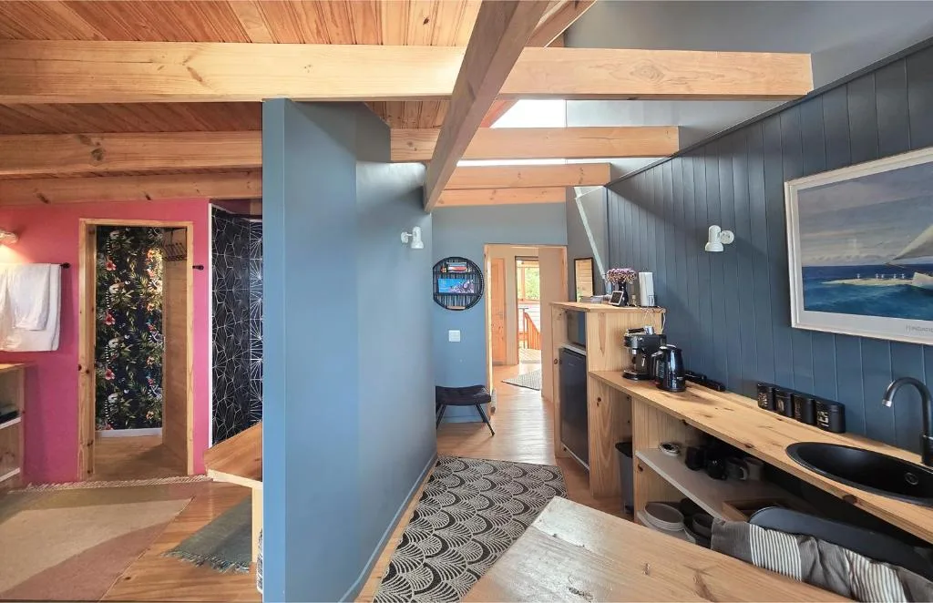 Modern open-plan interior with wooden beams, blue walls, and kitchenette