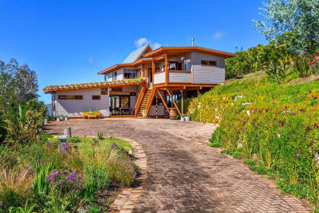 Modern elevated home with wooden accents and manicured gardens under blue sky