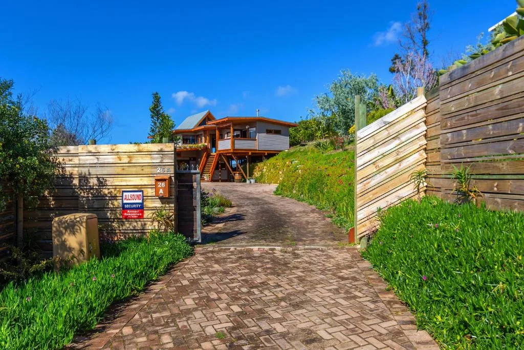Wooden elevated house with brick driveway, manicured hedges, and security gate