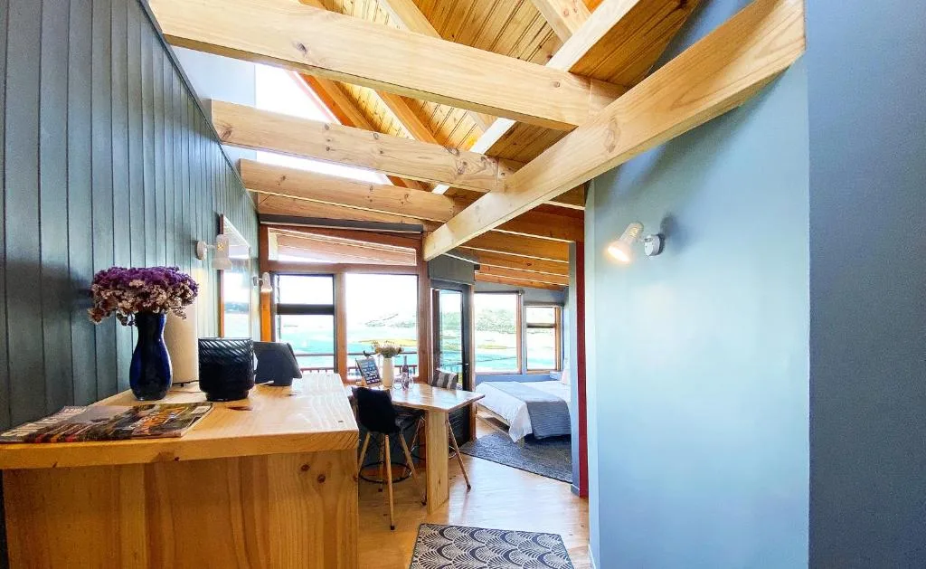 Modern open-plan lounge with wooden beams, blue walls, and lagoon views through large windows