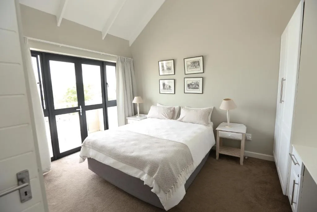 Bright bedroom with queen bed, bedside lamps, and black-framed glass doors