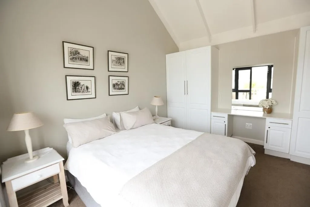Bright bedroom with queen bed, white wardrobe, and framed artwork on walls