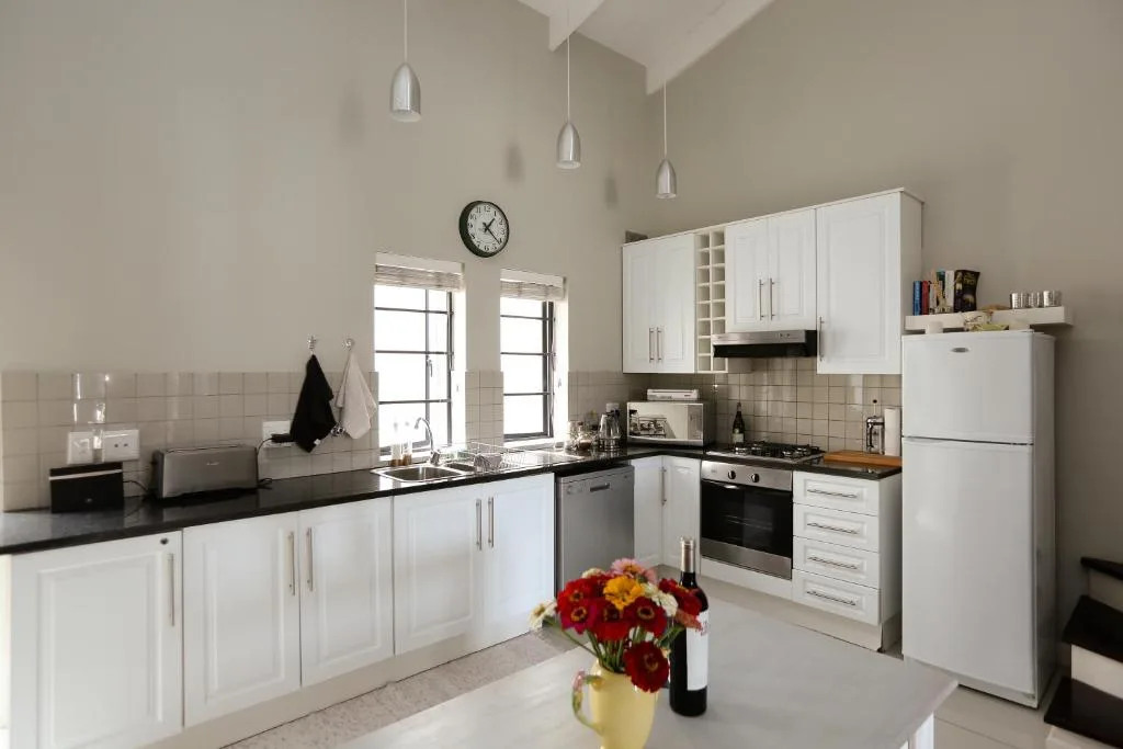 Modern white kitchen with black countertops, stainless steel appliances, and pendant lighting