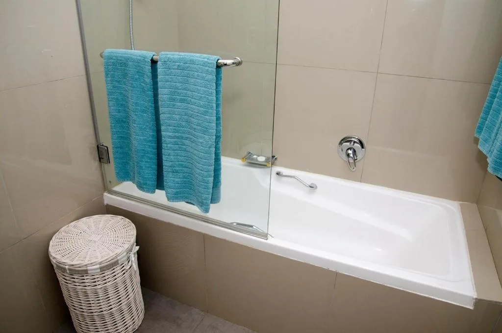 Modern bathroom with white bathtub, glass shower screen, and turquoise towels