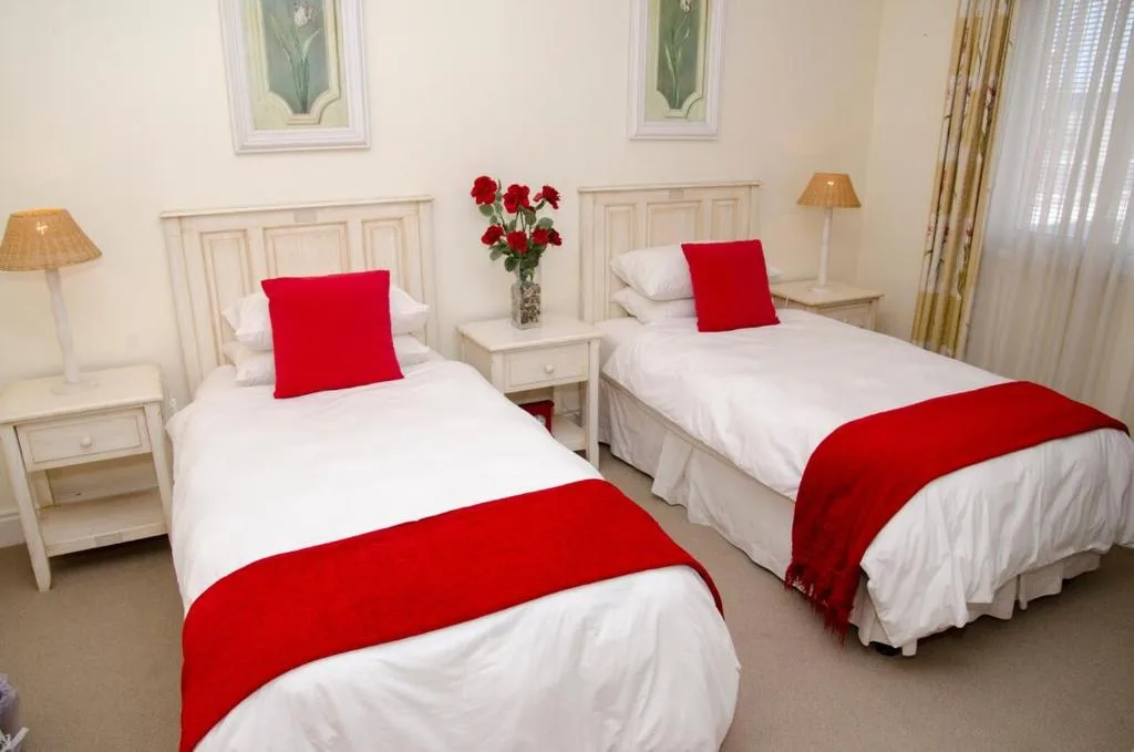 Twin bedroom with white linens, red accents, fresh flowers on bedside table
