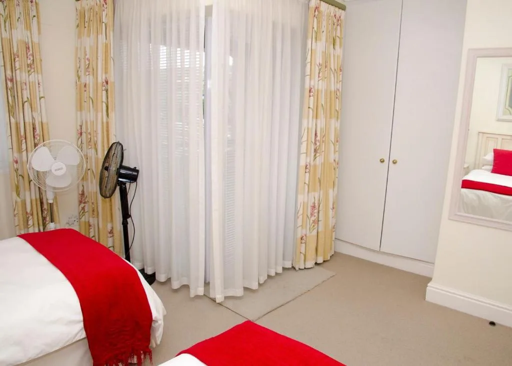Bright bedroom with twin beds, red accents, and garden views through windows