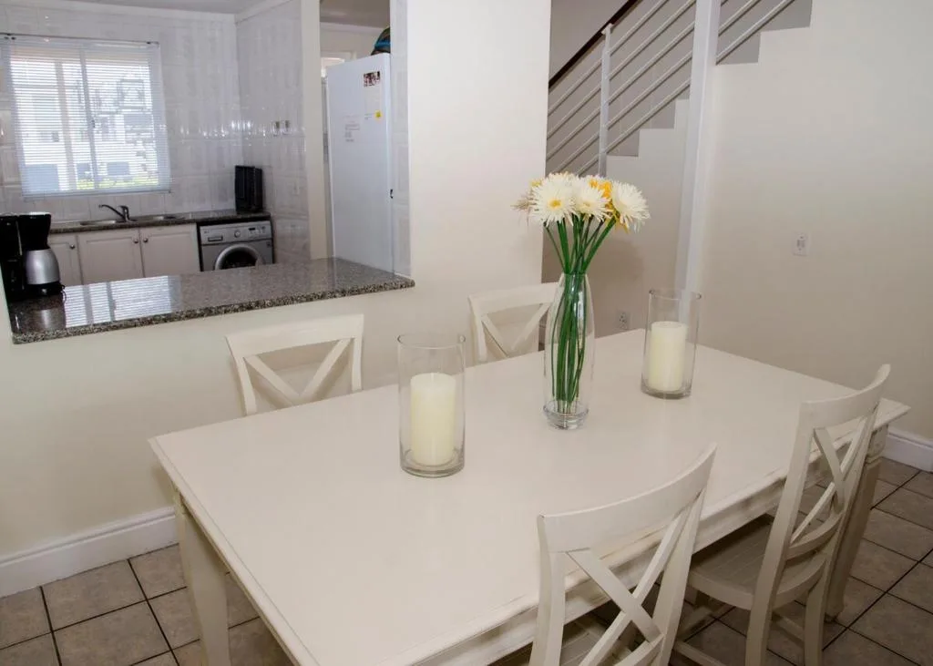 White dining table with chairs, fresh flowers, and candles in bright kitchen
