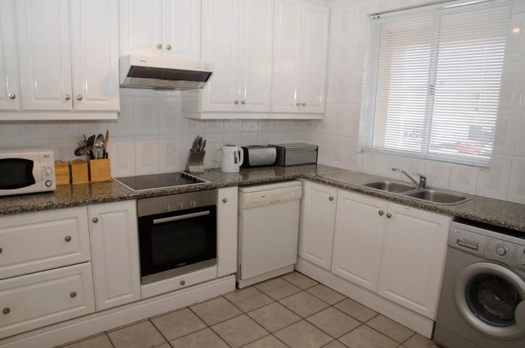 Modern white kitchen with granite counters, stove, and washing machine