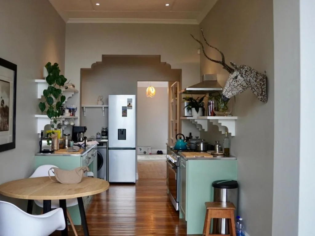Modern kitchen with mint cabinetry, stainless steel fridge, and open shelving with plants