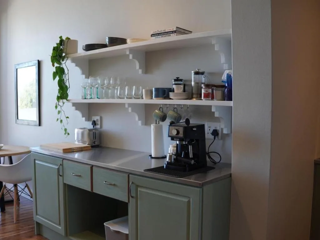 Modern kitchen with sage green cabinetry, open shelving, and espresso machine