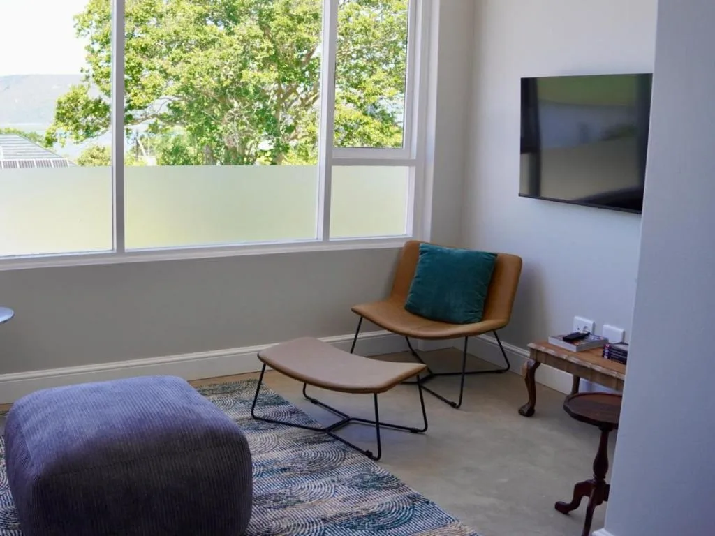 Modern lounge with tan armchair, ottoman, wall-mounted TV, and garden views