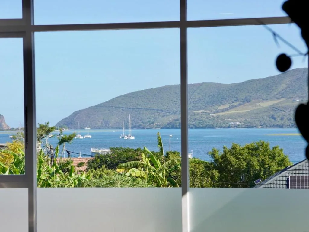 Blue lagoon with sailboats framed by large windows and lush vegetation