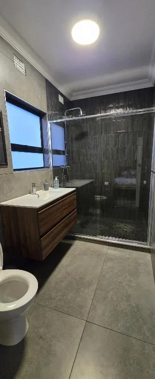 Modern bathroom with walk-in shower, wooden vanity, and toilet