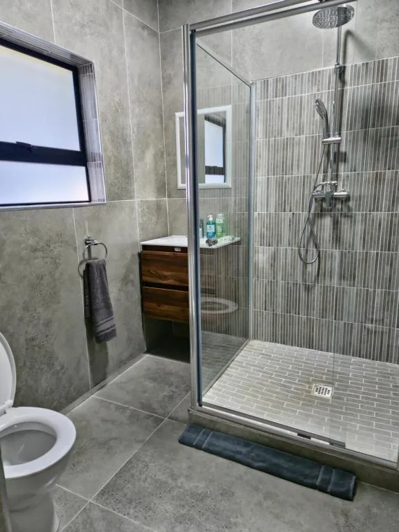 Modern bathroom with walk-in shower, gray tile walls, and white toilet