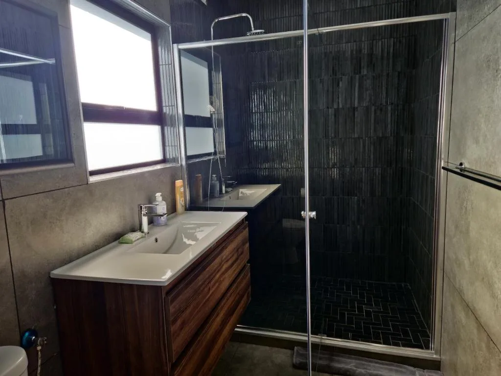 Modern bathroom with dark tile shower, wooden vanity, and natural light window