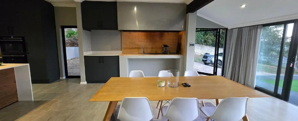 Modern dining table with white chairs adjacent to open-plan kitchen