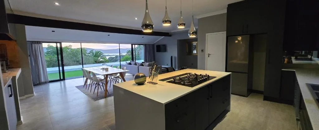 Modern open-plan kitchen with island cooktop, black cabinetry, and lagoon views