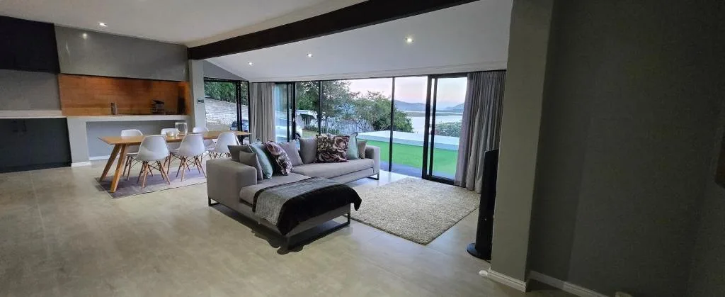 Modern lounge with grey sofa, dining area and water views through glass doors