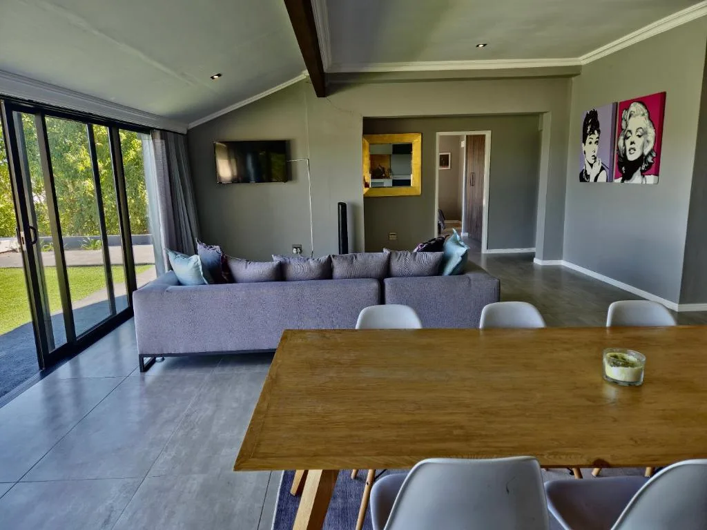 Open-plan lounge with grey sofa, dining table, garden views through sliding doors