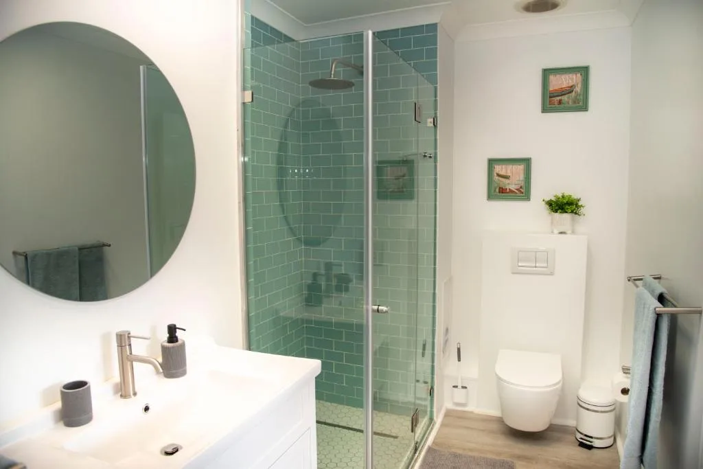 Modern bathroom with green subway tile shower and round mirror over vanity